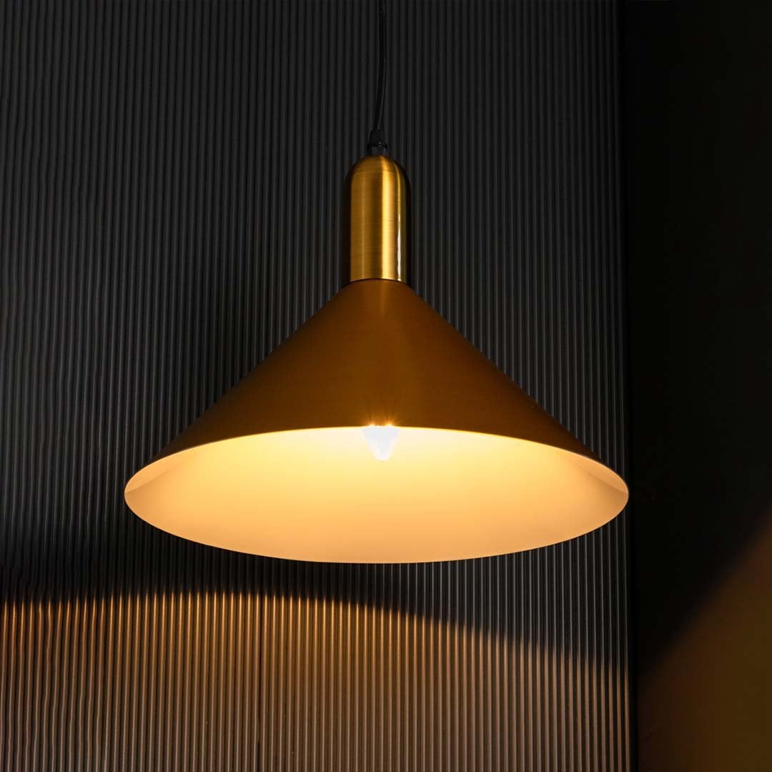 A gold cone pendant light with lights on casting warm downward illumination on a dark backdrop showcasing its wide shade and smooth finish.