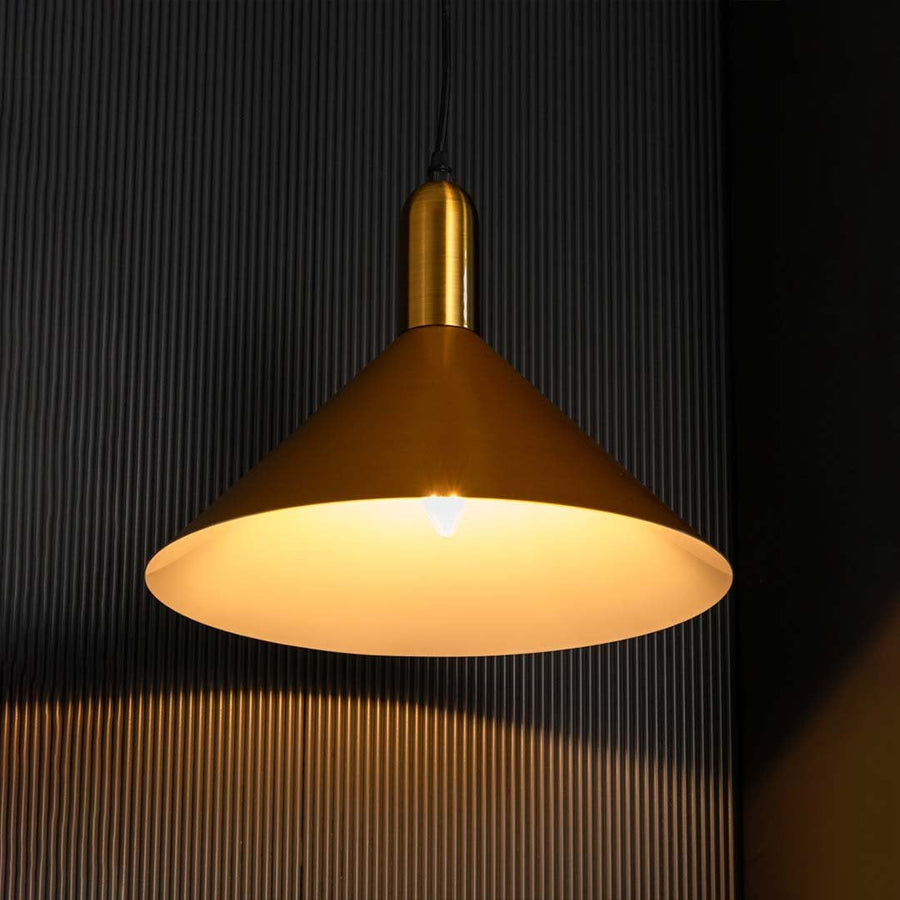 A gold cone pendant light with lights on casting warm downward illumination on a dark backdrop showcasing its wide shade and smooth finish.