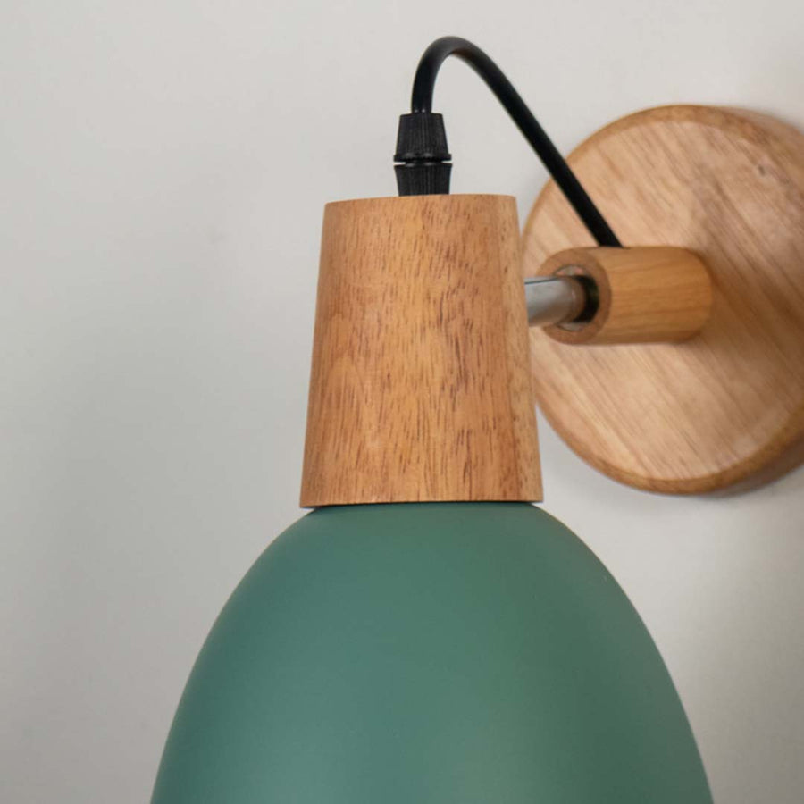 Closeup of wall lamp with matte green metal shade wooden base and black cord highlighting elegant modern wall sconce design.