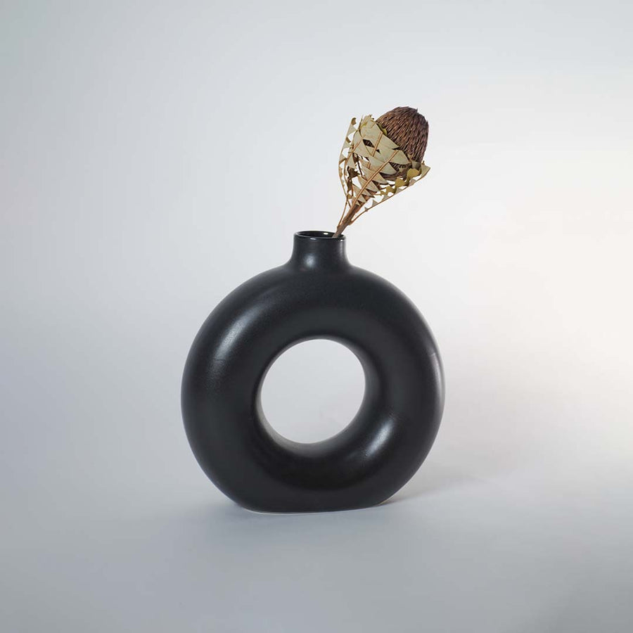 Modern black ceramic donut vases styled with pampas grass placed on wooden console table against white wall panel decor.