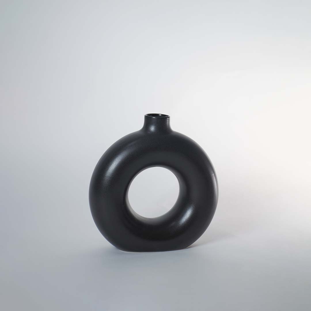A black circular vase photographed on a white background showing its smooth rounded silhouette and central hollow design that adds a modern artistic touch to decor.