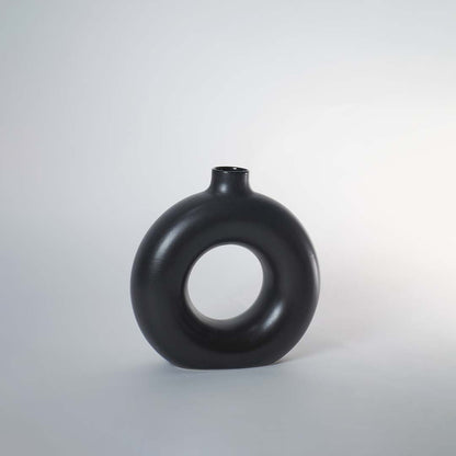 A black circular vase photographed on a white background showing its smooth rounded silhouette and central hollow design that adds a modern artistic touch to decor.