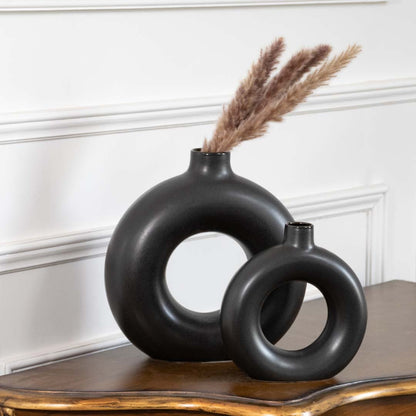 A pair of sleek black circular vases displayed on a classic wooden table enhancing the room with a clean sculptural look and soft natural decor elements.