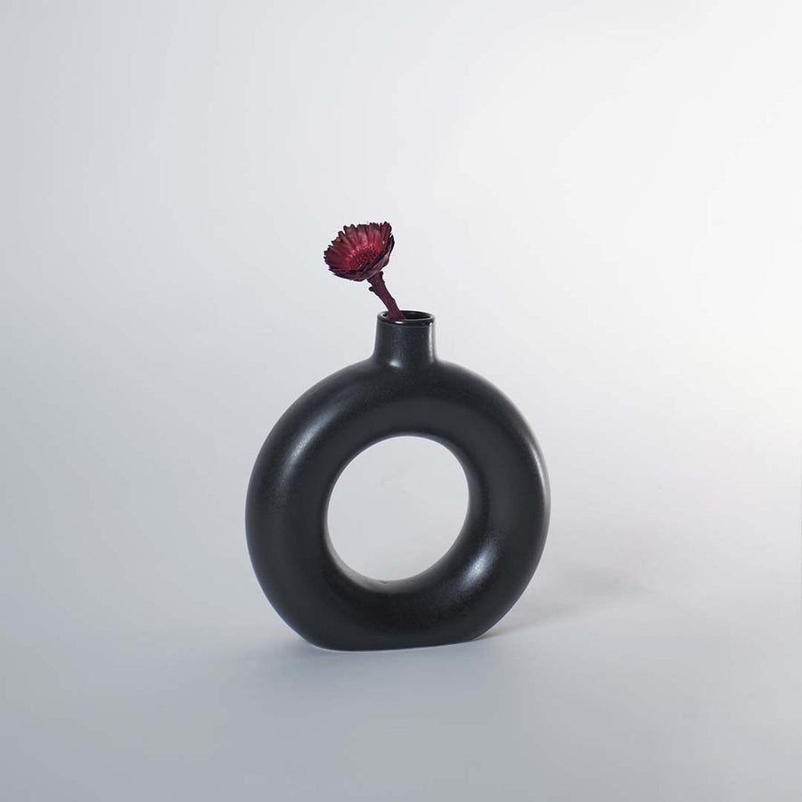 A modern round black decorative vase styled on a wooden tabletop with a larger matching vase beside it adding a sculptural accent to a bright elegant room.