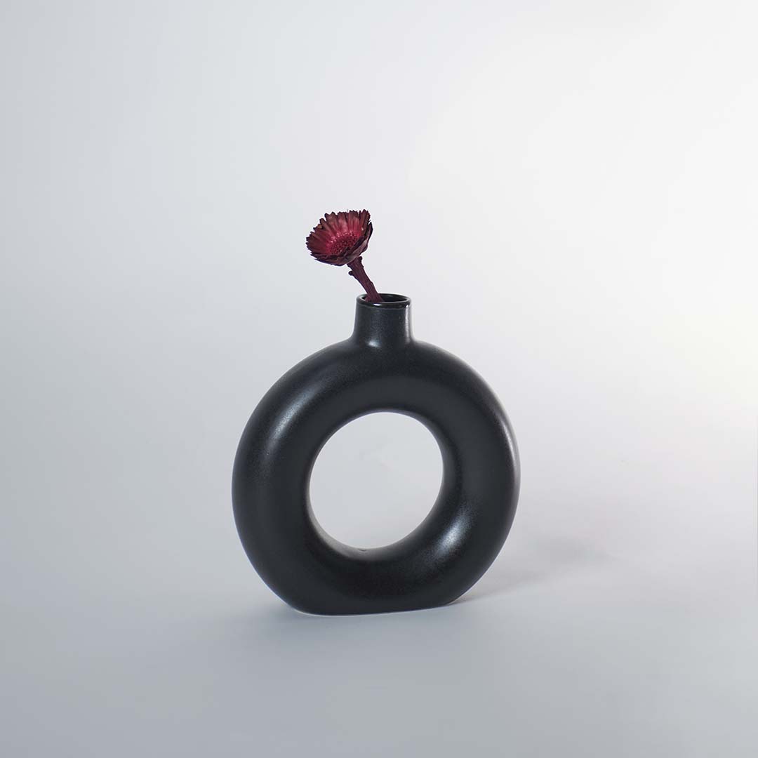 A modern round black decorative vase styled on a wooden tabletop with a larger matching vase beside it adding a sculptural accent to a bright elegant room.