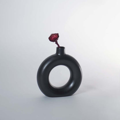 A modern round black decorative vase styled on a wooden tabletop with a larger matching vase beside it adding a sculptural accent to a bright elegant room.