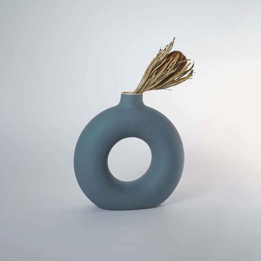 Modern green ceramic donut vase styled with dried stems placed on wooden console table for elegant home decor styling.