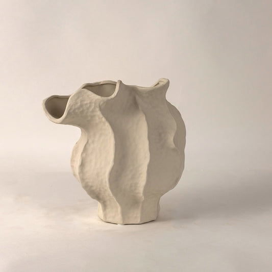 White ceramic vase with irregular curved sculptural form placed on white surface against neutral background highlighting contemporary artistic home decor appeal.
