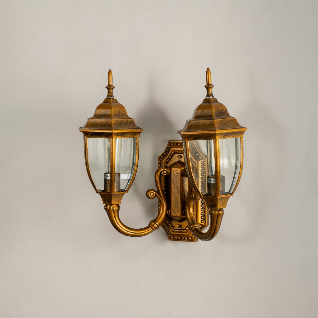 Antique brass double outdoor lantern on white background with lights off showing elegant curved design clear glass panels and decorative metal detailing.