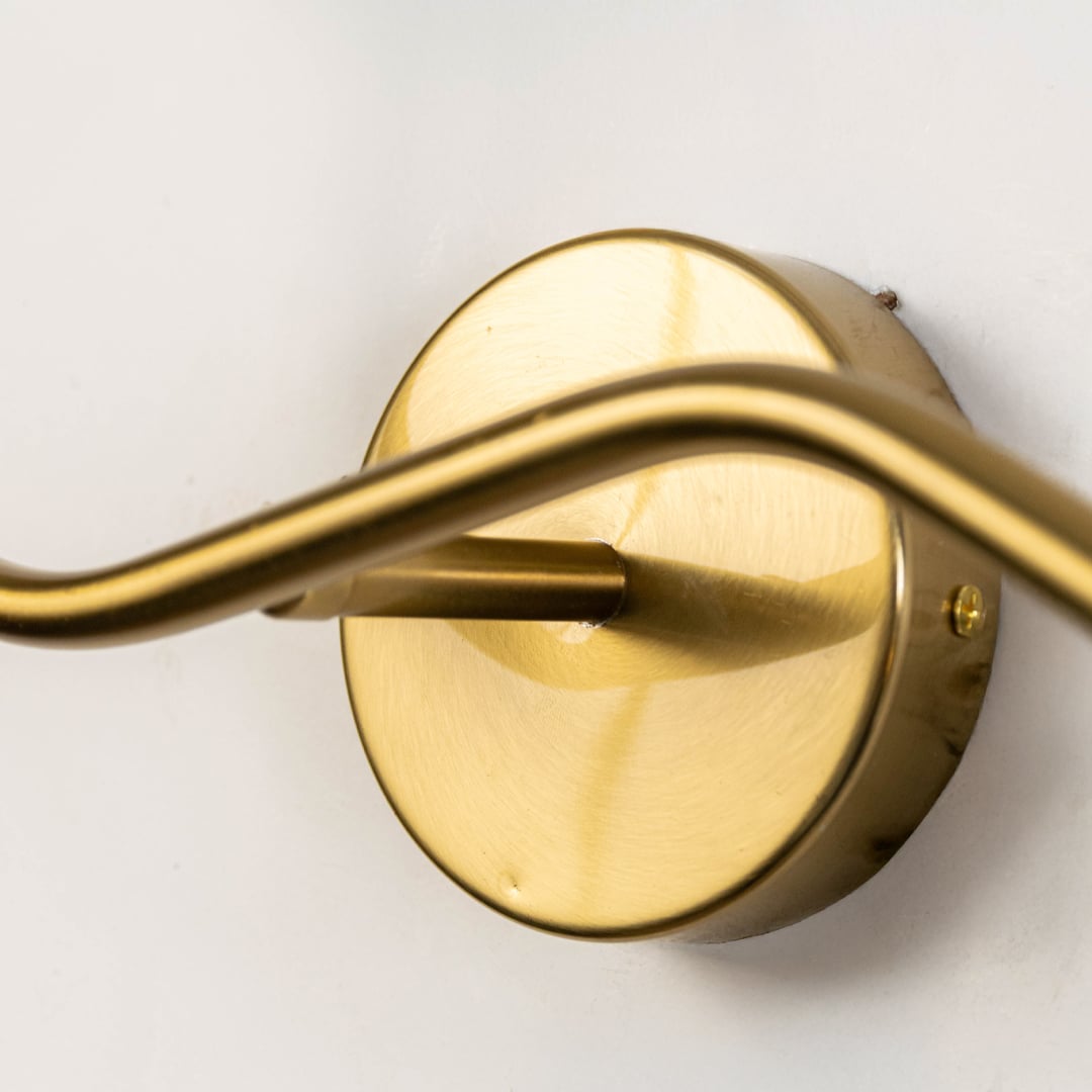 Closeup of double arm wall lamp with clear glass globes and gold metal fixture showing modern elegant home lighting design.