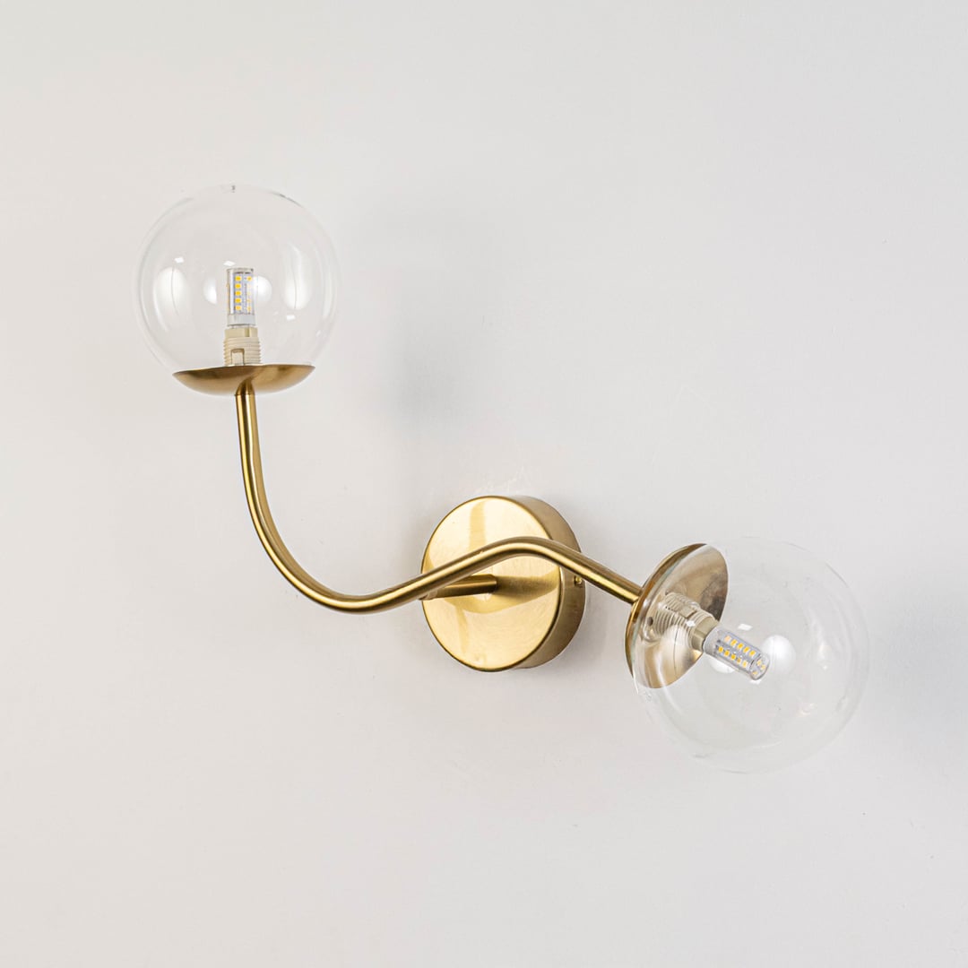 Double arm wall sconce with clear glass globes and gold base light off on white background stylish wall lighting for dining area.