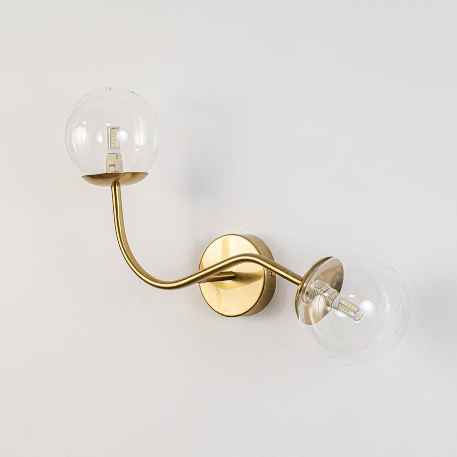 Double arm wall sconce with clear glass globes and gold base light off on white background stylish wall lighting for dining area.