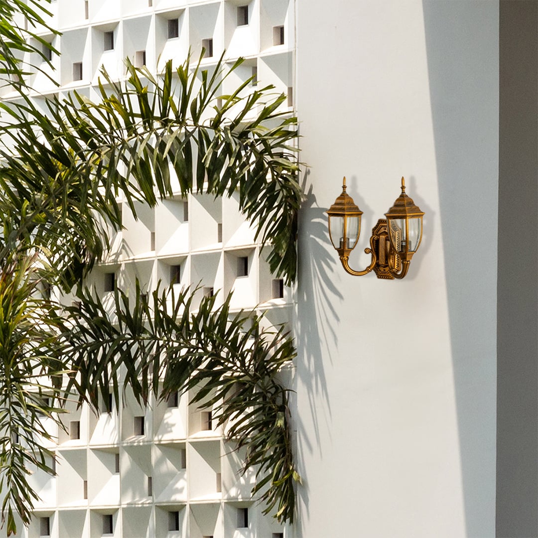 Double brass outdoor lantern with lights off fixed on a bright exterior wall featuring clear glass panels and antique brass finish for classic outdoor decor.