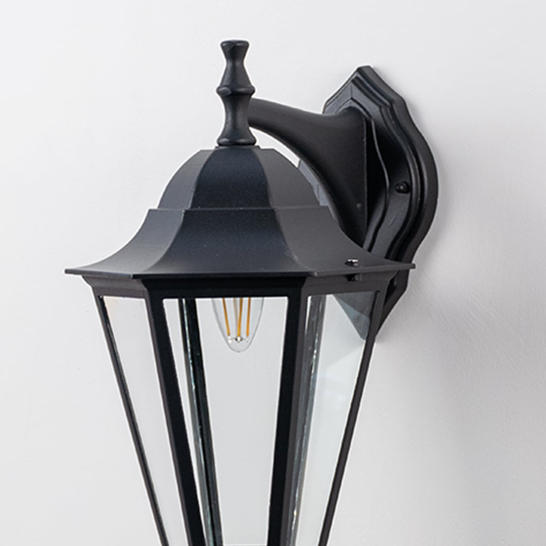 Closeup of decorative outdoor wall lantern with sleek black metal frame and clear glass panels showcasing bulb design.