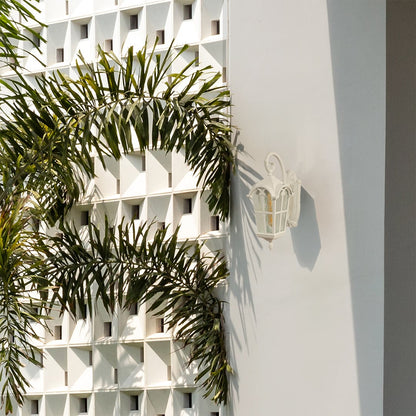 White outdoor wall light mounted on a sunlit exterior wall adding a refined decorative touch to a modern architectural facade with surrounding greenery.