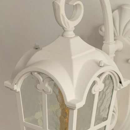 Closeup view of a white outdoor wall light showcasing its arched frame textured glass panels and decorative scroll detailing on the mounting arm.