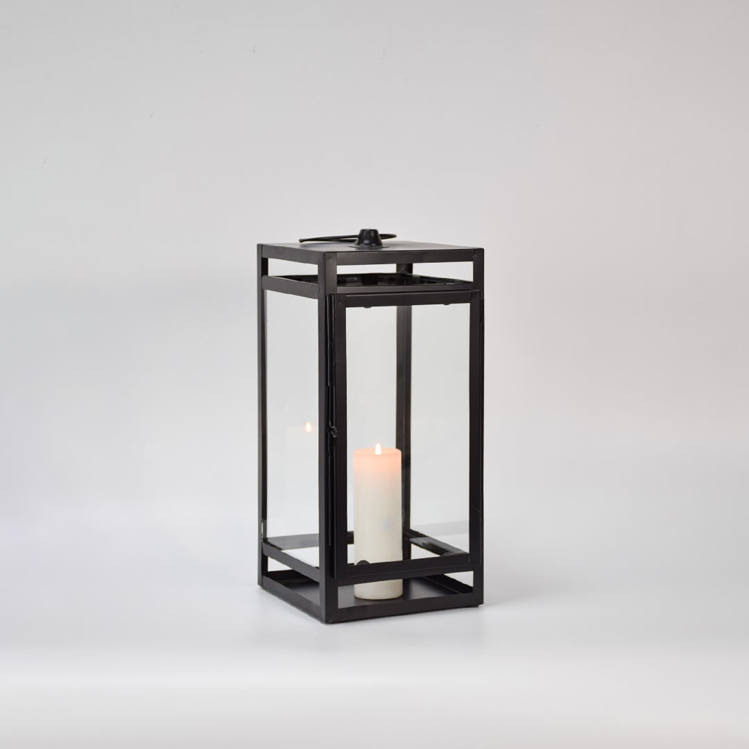Black metal glass lantern with candle burning on white background enhancing warm glow premium look and decorative atmosphere.