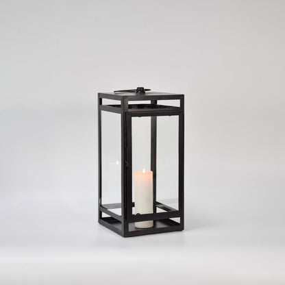 Black metal glass lantern with candle burning on white background enhancing warm glow premium look and decorative atmosphere.