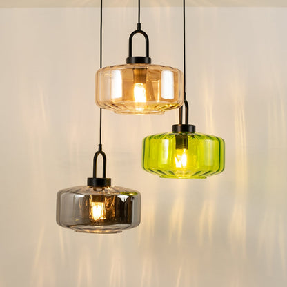 Three glass pendant lights in amber grey and green suspended together at staggered levels casting a warm glowing ambiance that enhances the modern room atmosphere.