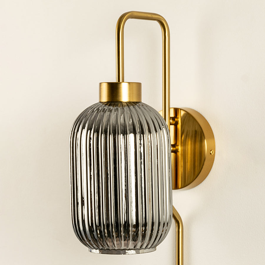 Closeup of gold metal wall light with ribbed glass shade showcasing detailed texture and premium finish for interior decor styling.