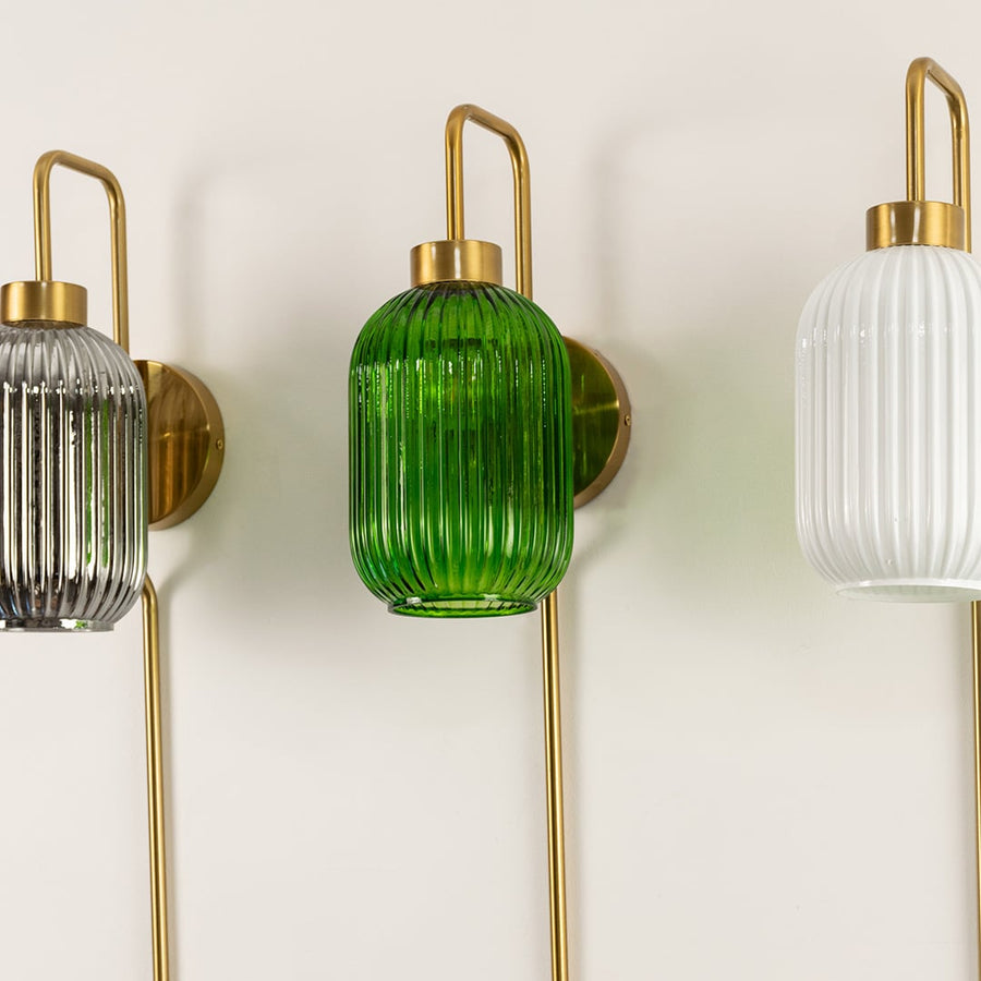 Three ribbed glass wall lights in grey green and white with brass handles and long brass rods mounted on a light wall shown up close.