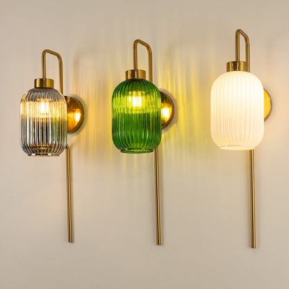 Three ribbed glass wall lights in grey green and white with brass handles and long brass rods mounted on a light wall each glowing softly.