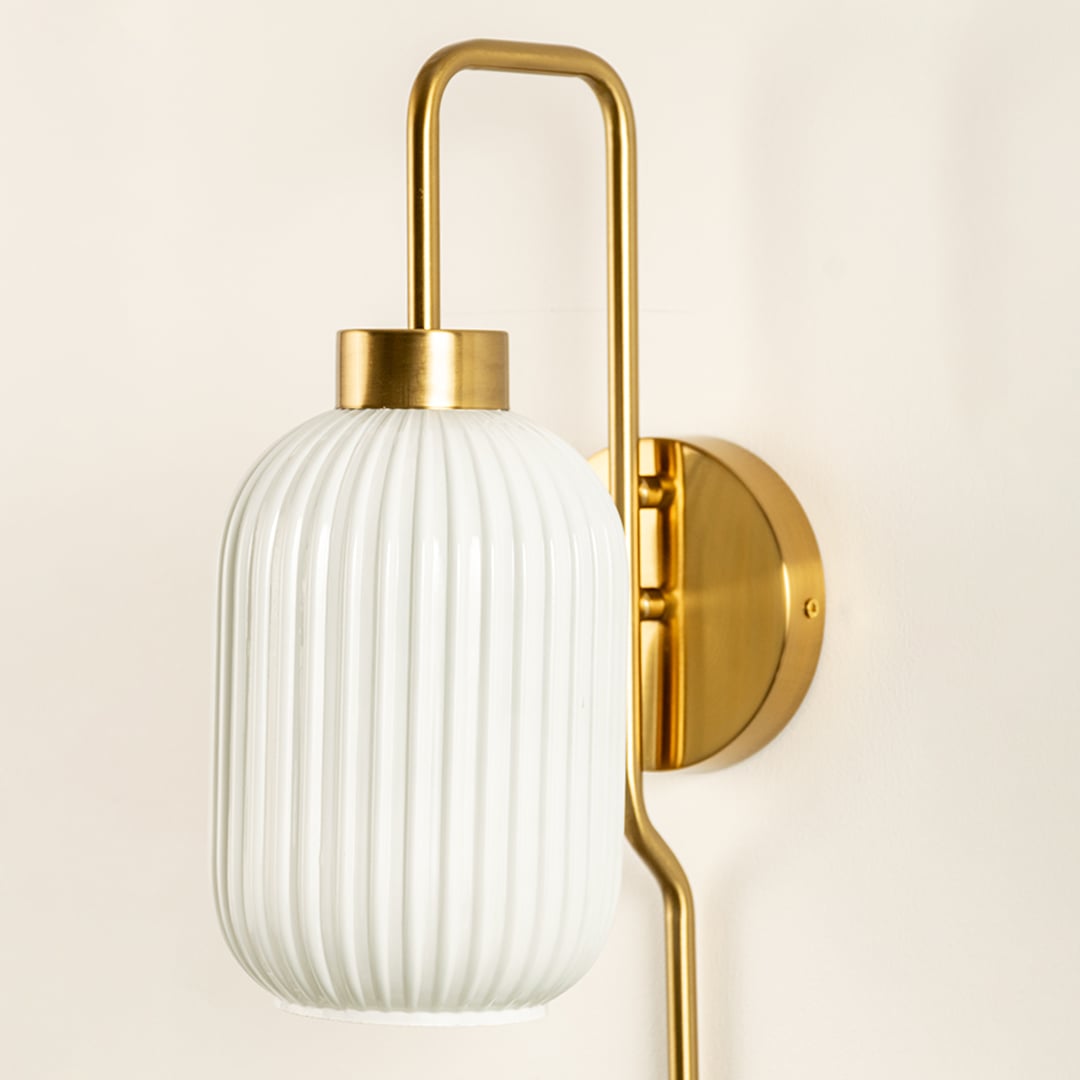 Closeup of ribbed white glass and gold metal wall light for premium bedroom and modern decor styling spaces.


