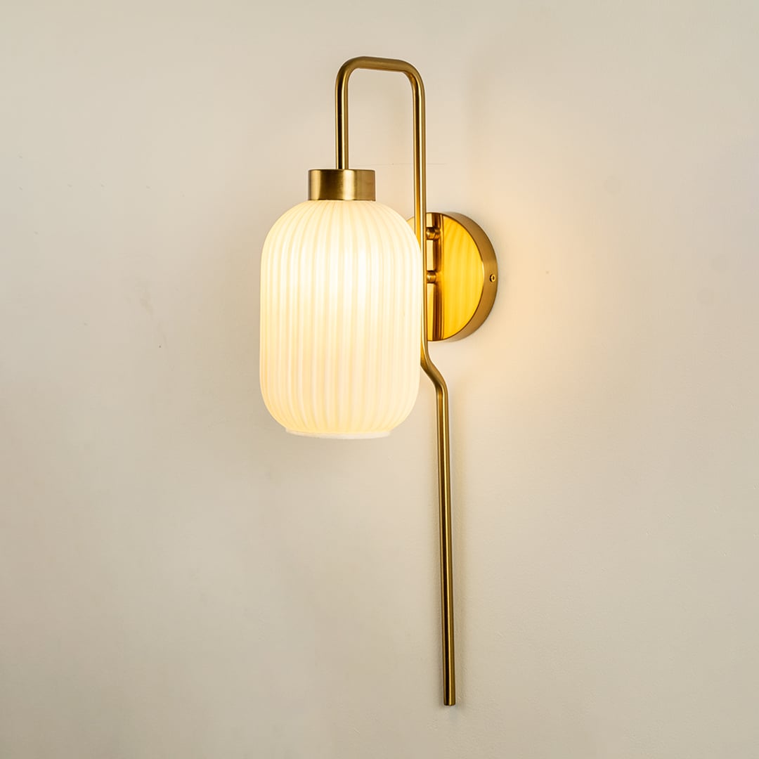 Gold metal wall light with white ribbed glass shade mounted vertically adding soft ambient lighting to modern interior Decor.
