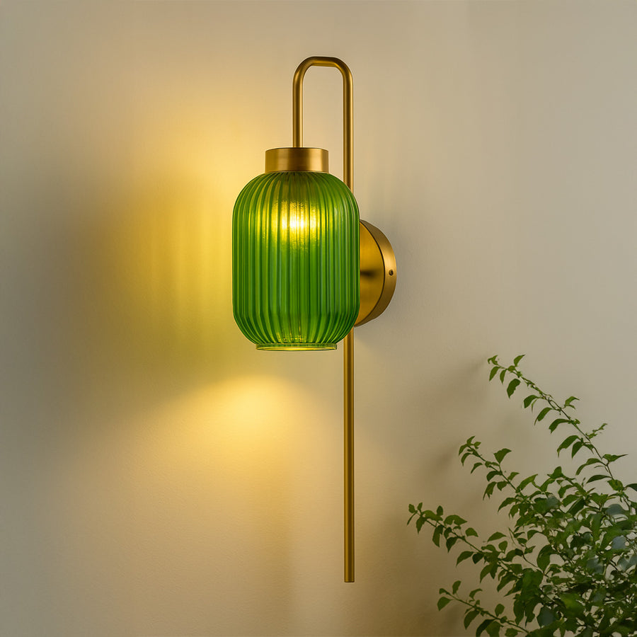 Gold metal wall light with green ribbed glass shade emitting warm glow ideal for bedroom or living room wall decor styling.