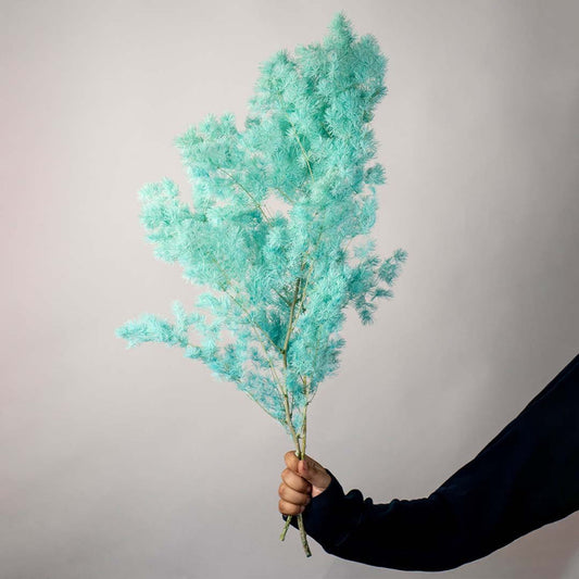 Hand holding a lush mint green dyed preserved tree grass foliage branch for vibrant modern dopamine decor on white backdrop.
