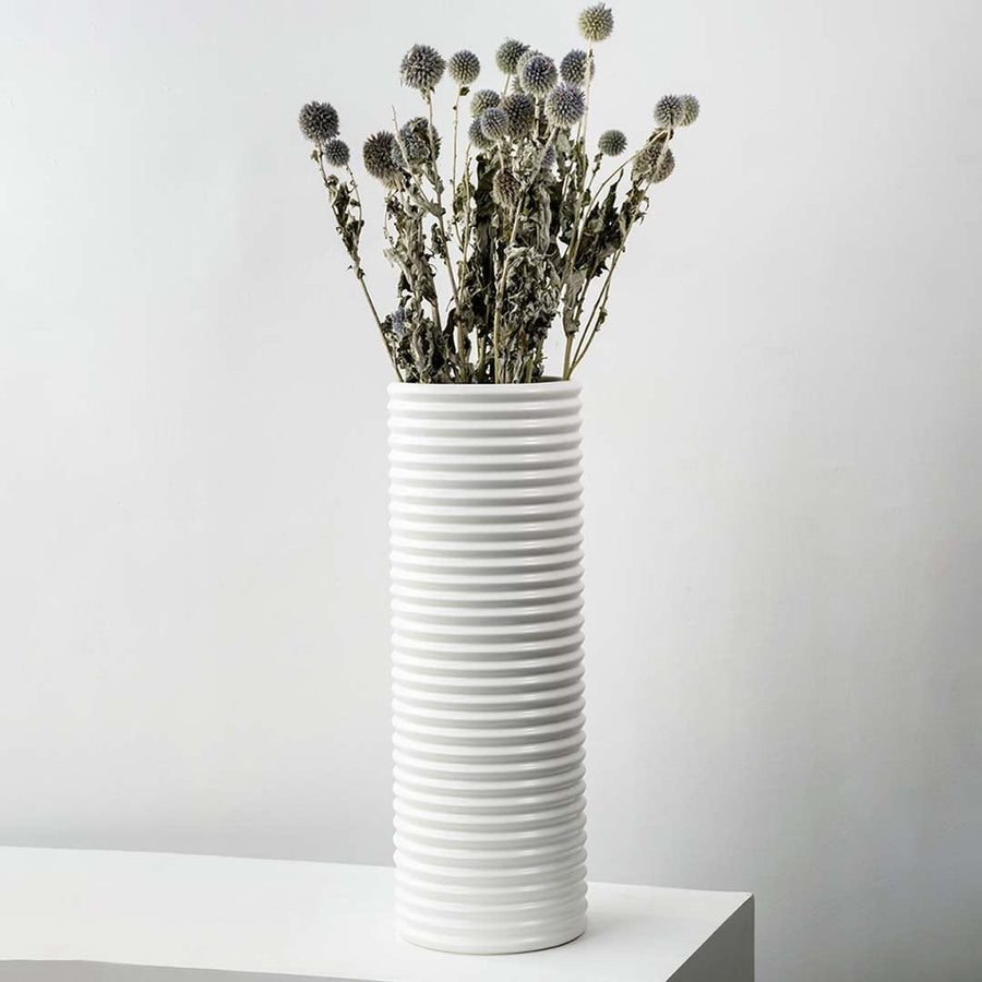 Grey dried globe thistle bouquet preserved flowers styled in tall white ceramic vase lifestyle modern home decor.