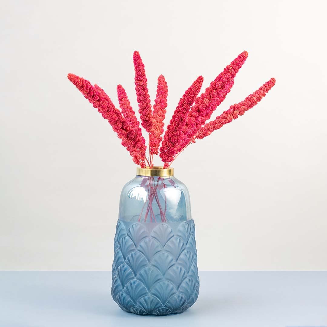 Vibrant pink dried millet stems styled in textured blue glass vase with gold rim creating modern lifestyle home decor.
