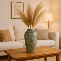 Fluffy beige dried pampas grass in a large ceramic vase on a wooden coffee table in front of a cozy living room couch.