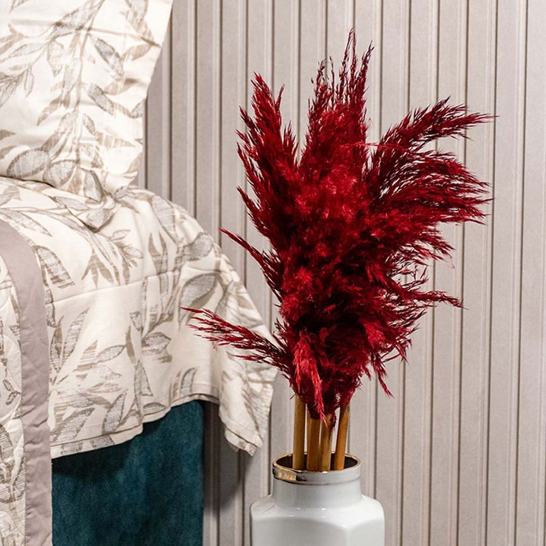 Closeup of dried floral arrangement with deep red pampas style stems placed in ceramic vase adding rich texture and warm decor accent.