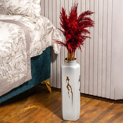Red pampas grass styled in tall white vase placed beside bed for modern home decor and luxury bedroom styling.