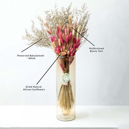 Pink bunny tails and beige dried grass floral bouquet mix arranged in a glass cylinder vase isolated on white background.