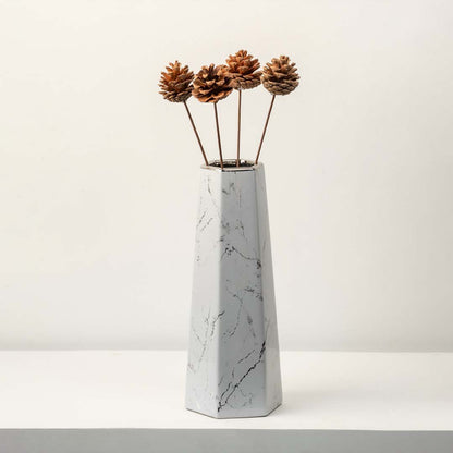 Four natural brown dried lotus seed pod stems arranged inside a modern grey marble geometric vase on a white tabletop backdrop.