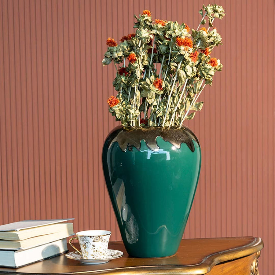 Glossy green ceramic vase with gold detailing and dried orange flowers styled in a cozy living room adding a rich artistic touch to modern interior decor.