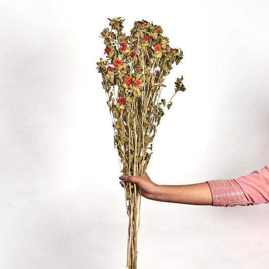 Hand holding a rustic dried wildflower bouquet featuring bright orange strawflower buds and green foliage stalks.