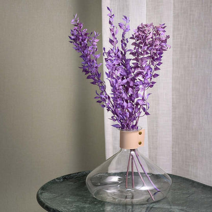 Purple preserved eucalyptus bunch in clear glass vase for modern home decor styling on a marble table.