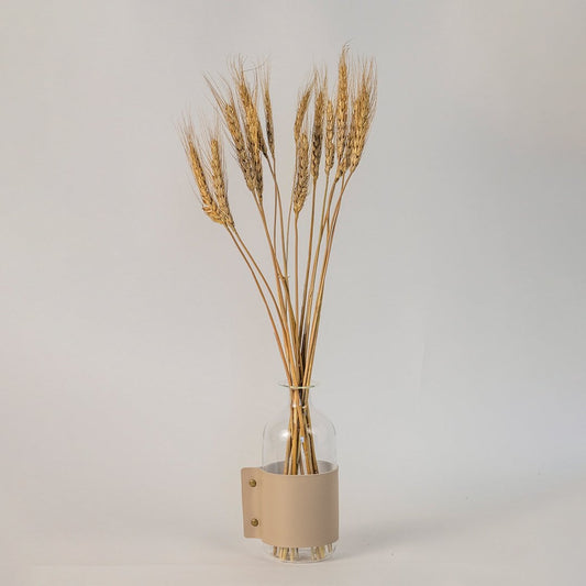 Dried wheat stems arranged in a clear glass vase with beige leather wrap creating a rustic and minimal home decor look.