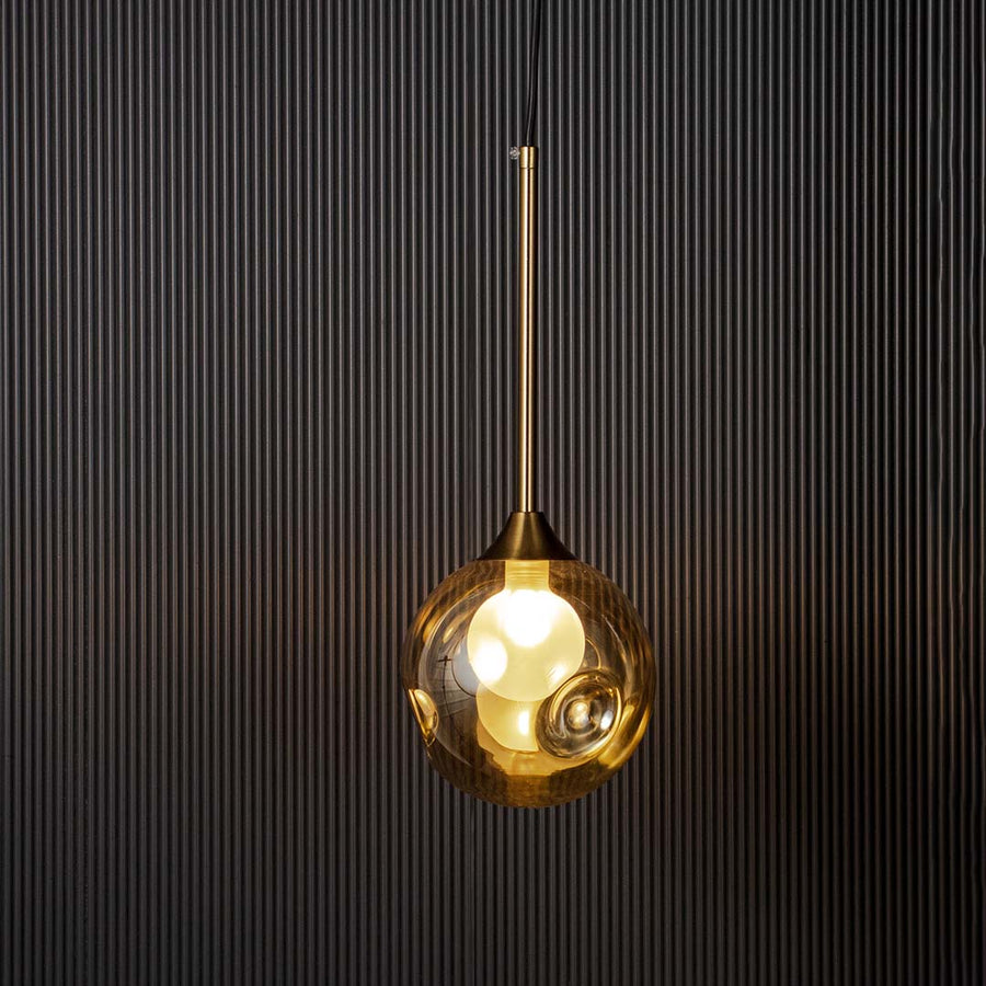 Amber glass globe pendant light glowing warmly with brass rod on black background perfect for living and dining areas.