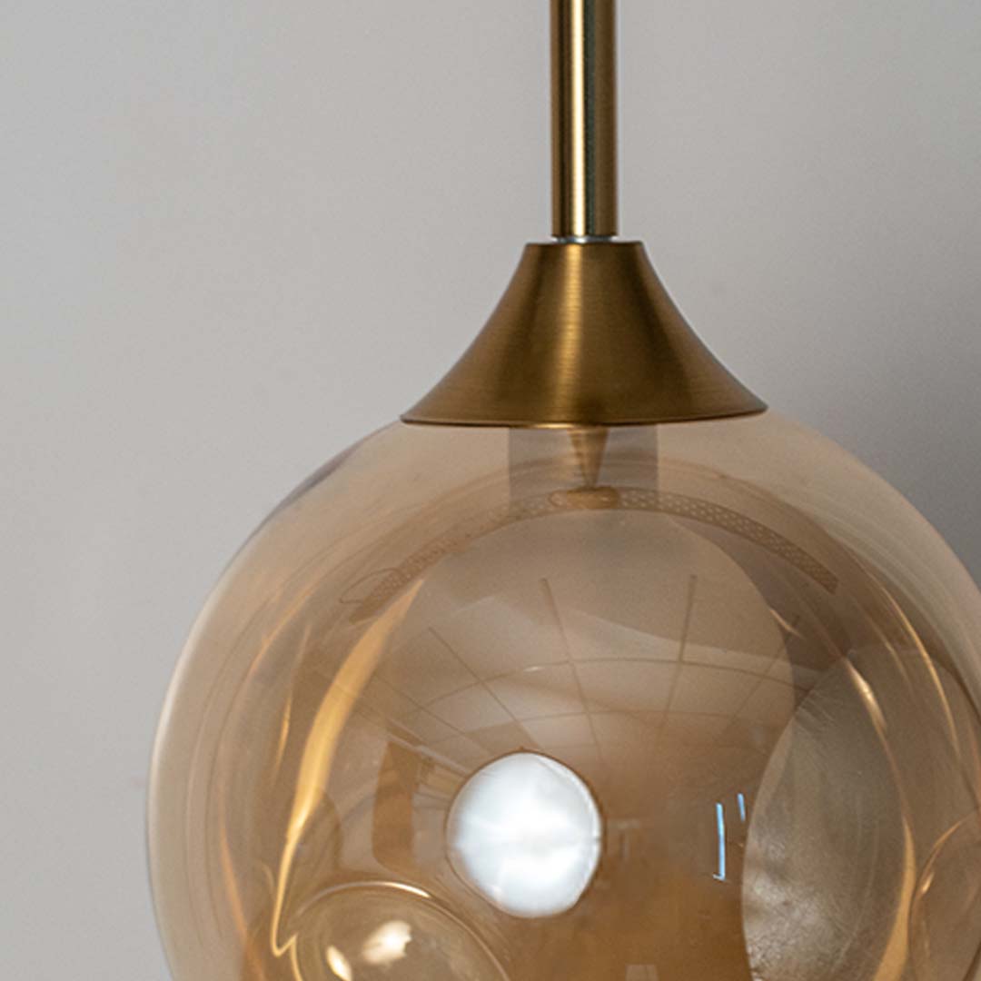 Closeup of amber glass globe pendant lamp with gold brass rod highlighting elegant finish and modern lighting style.