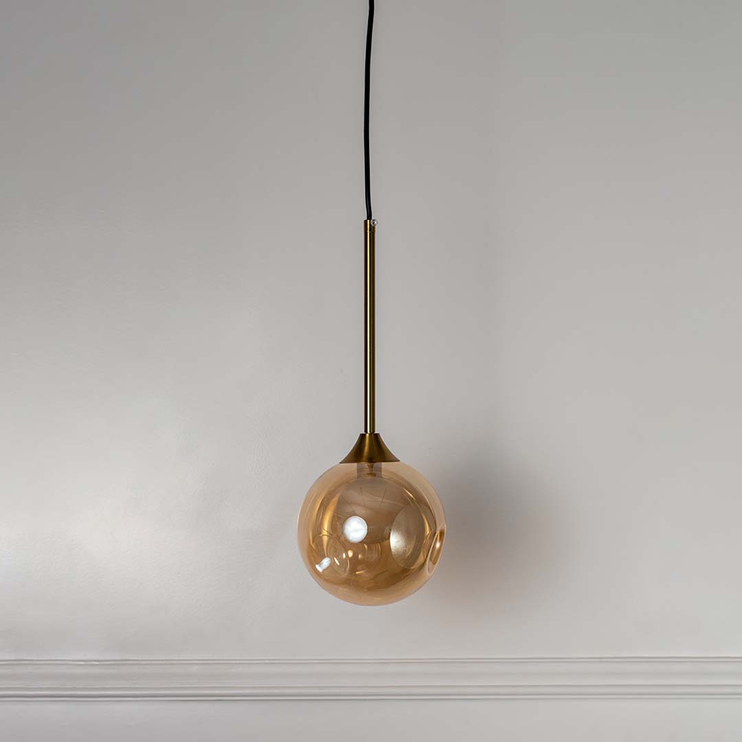 Modern amber glass globe pendant lamp with gold brass rod shown off on white background for home and dining decor.