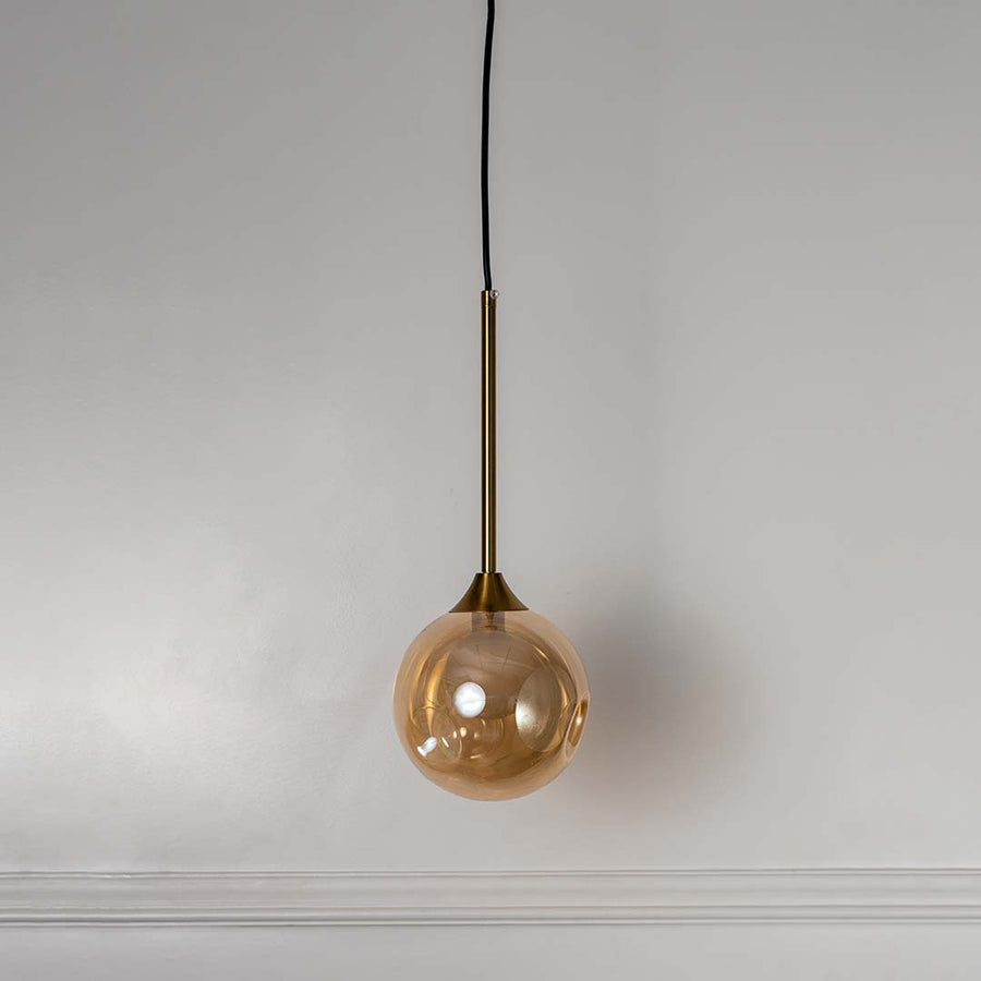 Modern amber glass globe pendant lamp with gold brass rod shown off on white background for home and dining decor.