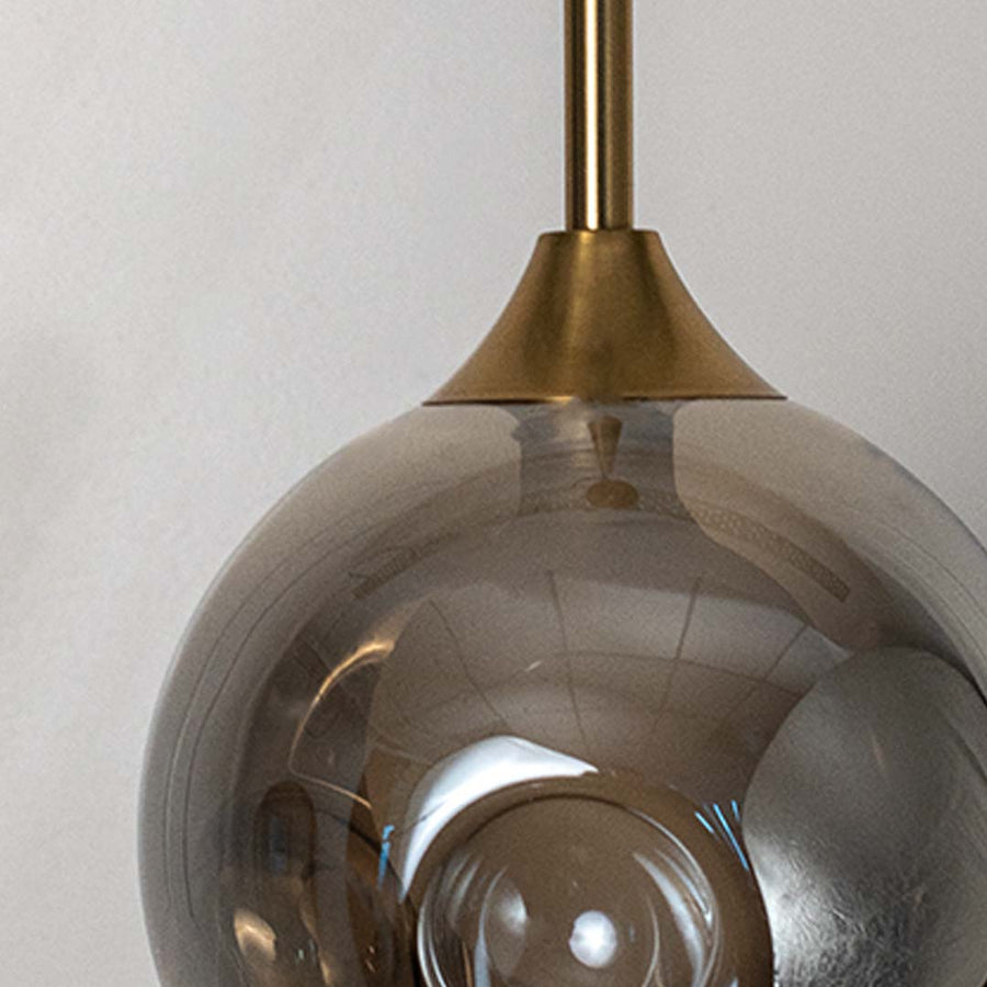 Closeup of smoked grey glass globe pendant lamp with gold brass rod highlighting elegant finish and premium design.