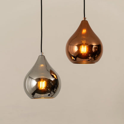 Two reflective teardrop pendant lights in silver and copper hanging from black cords with warm glowing bulbs inside against a light background.