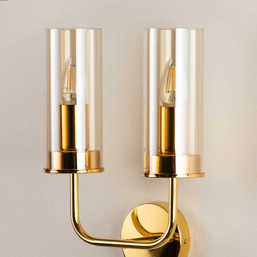 Contemporary brass metal wall light with dual clear glass shades for stylish modern interior wall decor.