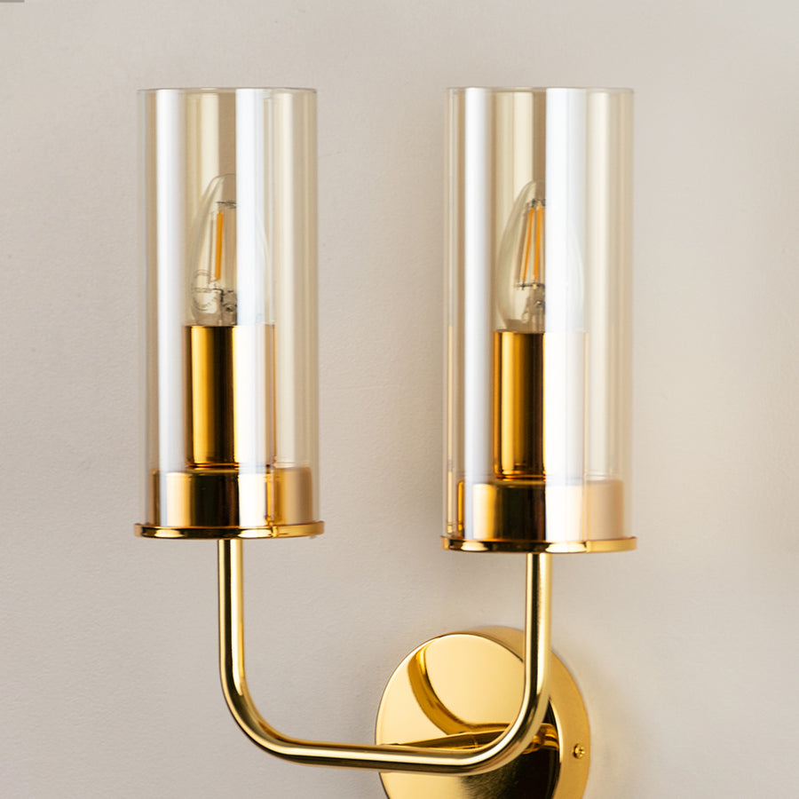 Contemporary brass metal wall light with dual clear glass shades for stylish modern interior wall decor.