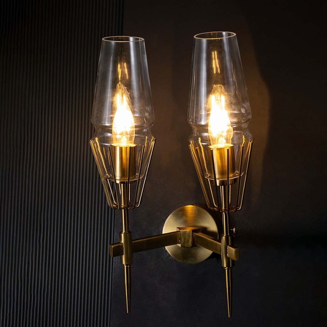 Glowing gold brass double wall light with glass shades set against black background emphasizing dramatic ambiance and luxury design.
